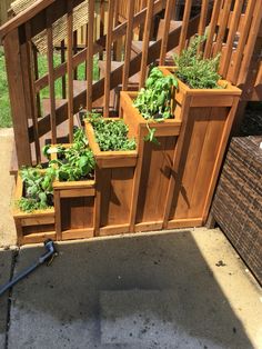 several wooden planters filled with green plants on the side of a house's porch