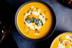 two bowls filled with carrot soup and topped with whipped cream, pumpkin seeds and green leaves