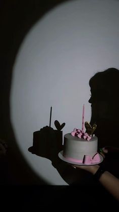 a person holding a cake with candles in the shape of hearts on it and a shadow behind them