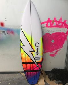 a surfboard leaning against a wall with graffiti on it's side and another painting in the background