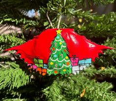 a christmas tree ornament hanging from a pine tree with presents on it's top