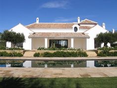 a large white house with a pool in front of it and trees around the perimeter