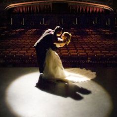 a bride and groom dance on the floor in front of an empty stage at night