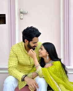 a man and woman sitting next to each other in front of a pink wall with white trim