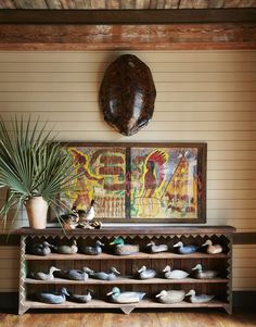 a wooden shelf with shoes on it in front of a painting and potted plant