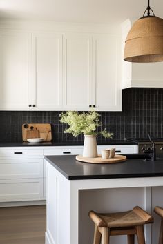 a kitchen with white cabinets and black counter tops, two stools in front of the island