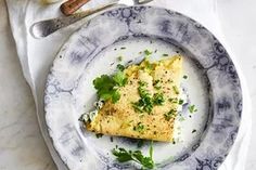 an omelet with parsley on a blue and white plate next to utensils