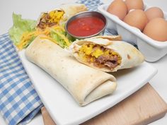 a burrito on a plate next to eggs and ketchup