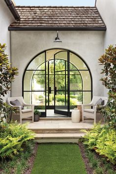 an arched glass door with two chairs in front of it and grass on the ground