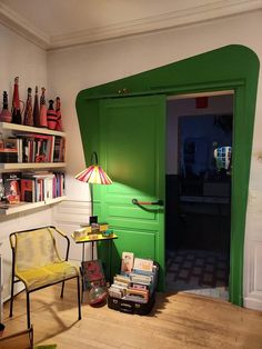 a green door is open in a room with chairs and books on the shelf next to it