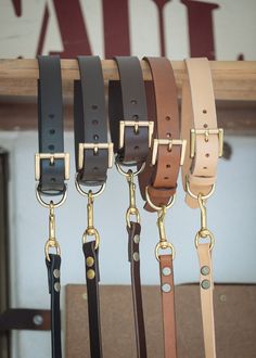 several different colored belts hanging up on a wooden rack with gold hardware and brass fittings