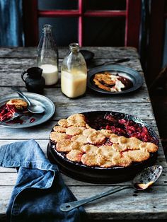 a wooden table topped with a pie next to a bottle of milk and two plates filled with food