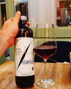 a person holding a bottle of wine next to a glass of red wine on a wooden table