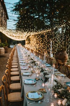 a long table is set with candles, plates and place settings for an outdoor dinner