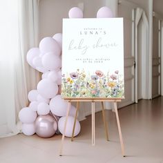 a baby shower sign next to balloons in a room with white walls and flooring