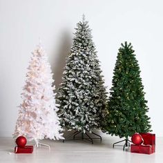 three artificial christmas trees are lined up on the floor next to each other with presents under them