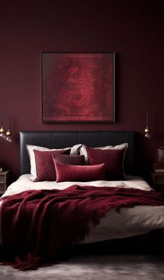 a bed with red pillows and blankets in a dark colored room, next to a painting on the wall