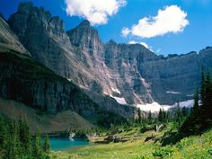 the mountains are covered in snow and green grass, with trees on either side of them