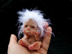 a hand holding a small doll with white hair on it's head and fingers