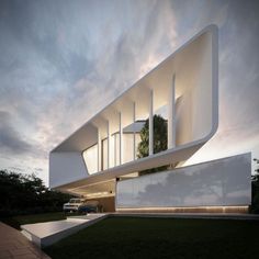 an architecturally designed white building on the side of a road at dusk with clouds in the background