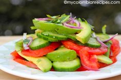 a white plate topped with cucumber, tomatoes and red onion wedges on top of a wooden table