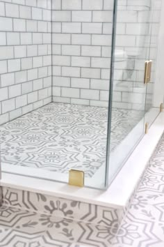 a bathroom with white tile and gold accents on the shower door, which is decorated in black and white tiles