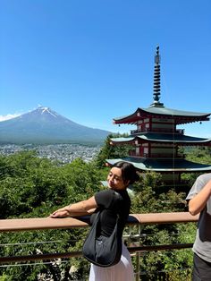 two people are standing on a balcony looking at the mountains and pagodas in the distance