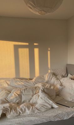 an unmade bed with white sheets and pillows in a room that has sunlight streaming through the windows