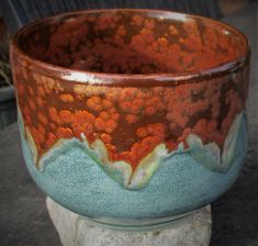 a brown and blue bowl sitting on top of a stone slab next to a planter