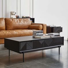 a brown leather couch sitting next to a table with books on it in front of a white wall