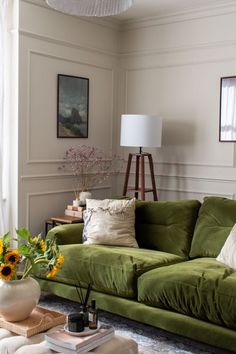 a living room with green couches and sunflowers on the coffee table in front of it