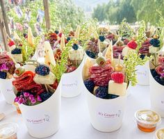 several cups filled with different types of food on a white tablecloth covered outdoor area