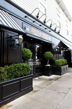 the outside of a restaurant with potted plants on the sidewalk