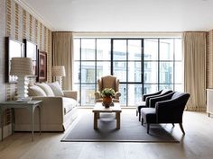 a living room filled with furniture next to a large glass window covered in curtains and drapes