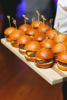 mini burgers are lined up on a wooden tray with toothpicks stuck in them