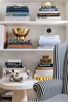 a white table topped with books next to a chair and a shelf filled with books