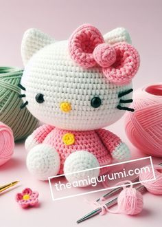 a crocheted hello kitty sitting next to balls of yarn and knitting needles on a pink surface