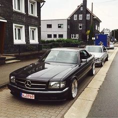 two cars parked next to each other on the side of a street with houses in the background