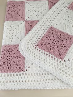 two pink and white crocheted afghans sitting on top of a table next to each other