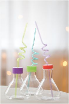 three glass bottles with colorful straws in them sitting on a table next to each other