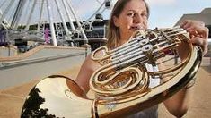 a woman holding a large brass instrument in front of a ferris wheel