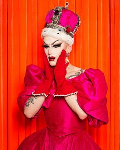 a woman in a red dress with a crown on her head and hands near her face