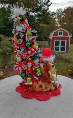 a small christmas tree on top of a table in front of a red barn and trees