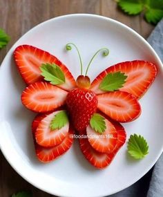 a white plate topped with strawberries and a butterfly shaped piece of fruit on top of it