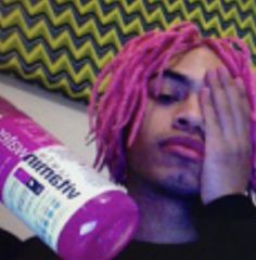 a young man with pink dreadlocks holding a bottle of hair paste in front of his face