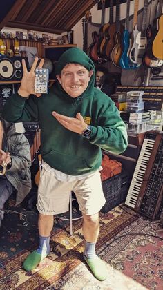 a man in a green hoodie is giving the peace sign with his hand while standing in front of guitars