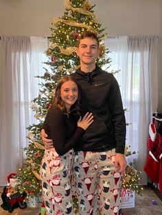 a man and woman standing in front of a christmas tree with their arms around each other