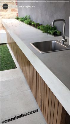 an outdoor kitchen with concrete counter tops and stainless steel sink faucet, grass growing on the wall