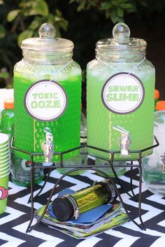 there are two jars with green liquid on the table next to each other and cups