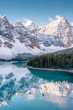 the mountains are covered in snow and there is a body of water with two canoes on it